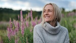 Une femme ayant pris du shilajit, du shilajit pur, du shilajit en bocal et du shilajit resine sourit au milieu de fleurs sauvages roses sous un ciel nuageux.